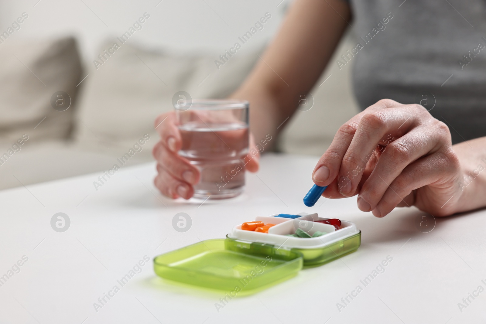 Photo of Woman with pills, organizer and glass of water at white table, closeup