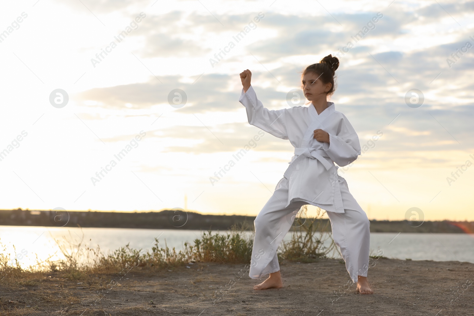 Photo of Cute little girl in kimono practicing karate near river at sunset