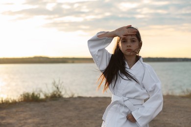 Photo of Cute little girl in kimono practicing karate near river at sunset