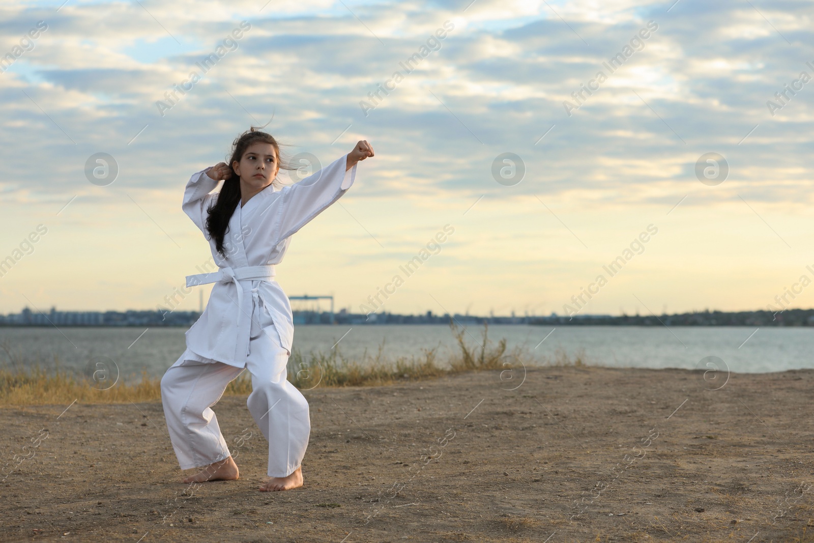 Photo of Cute little girl in kimono practicing karate near river