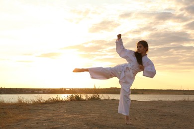 Photo of Cute little girl in kimono practicing karate near river at sunset