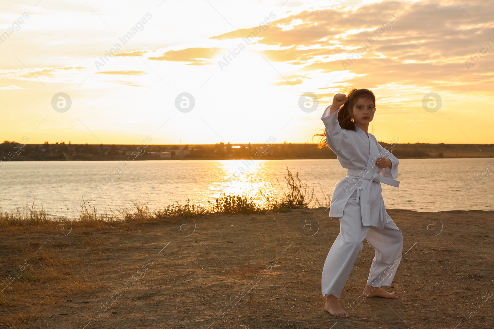 Photo of Cute little girl in kimono practicing karate near river at sunset