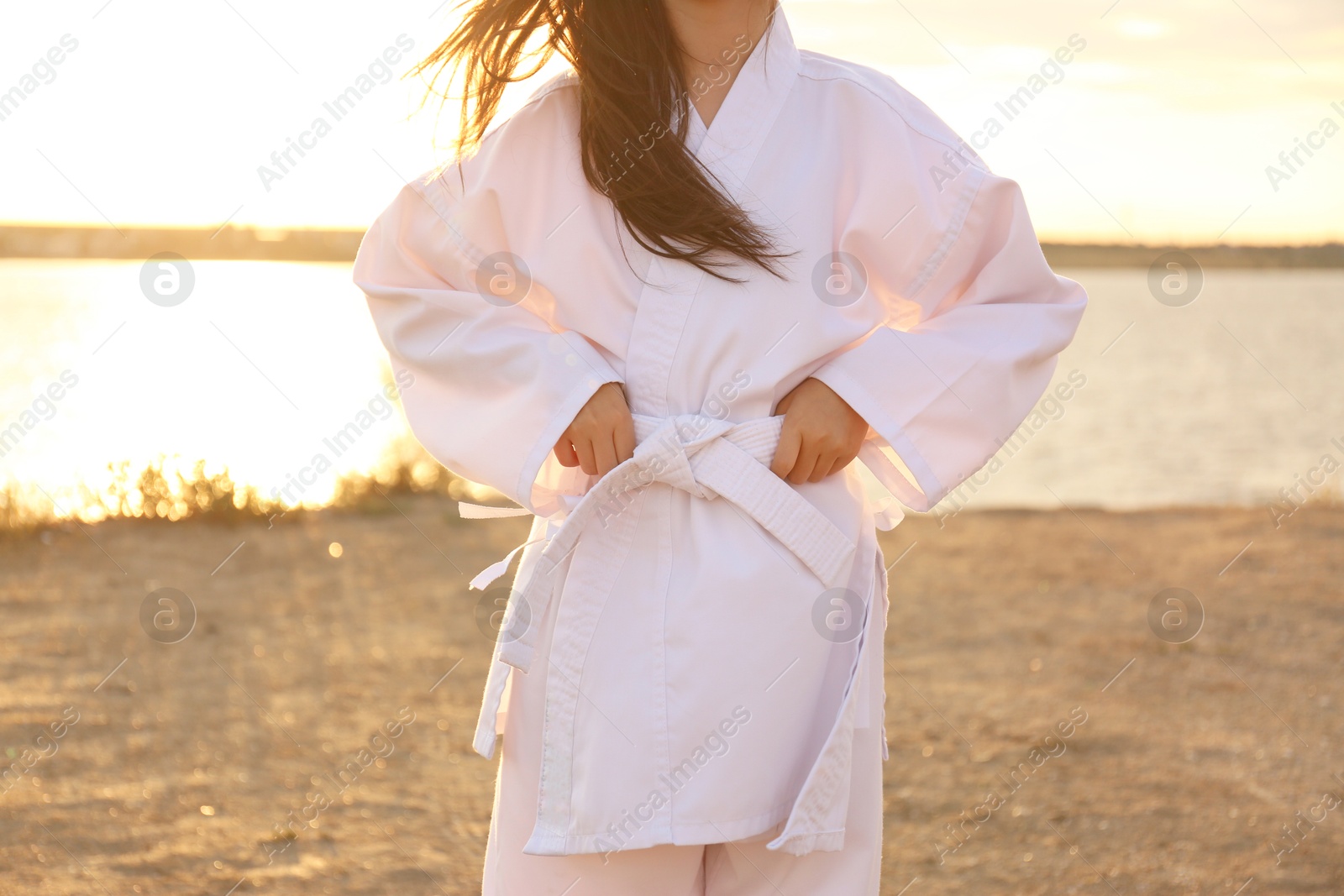 Photo of Cute little girl in kimono near river at sunset, closeup. Karate practicing