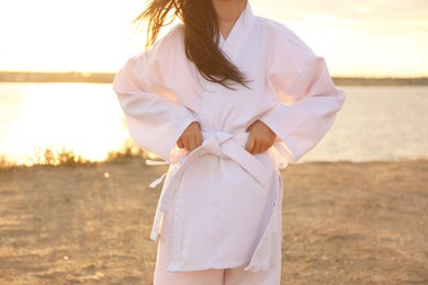 Cute little girl in kimono near river at sunset, closeup. Karate practicing