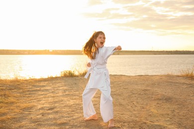 Photo of Cute little girl in kimono practicing karate near river at sunset