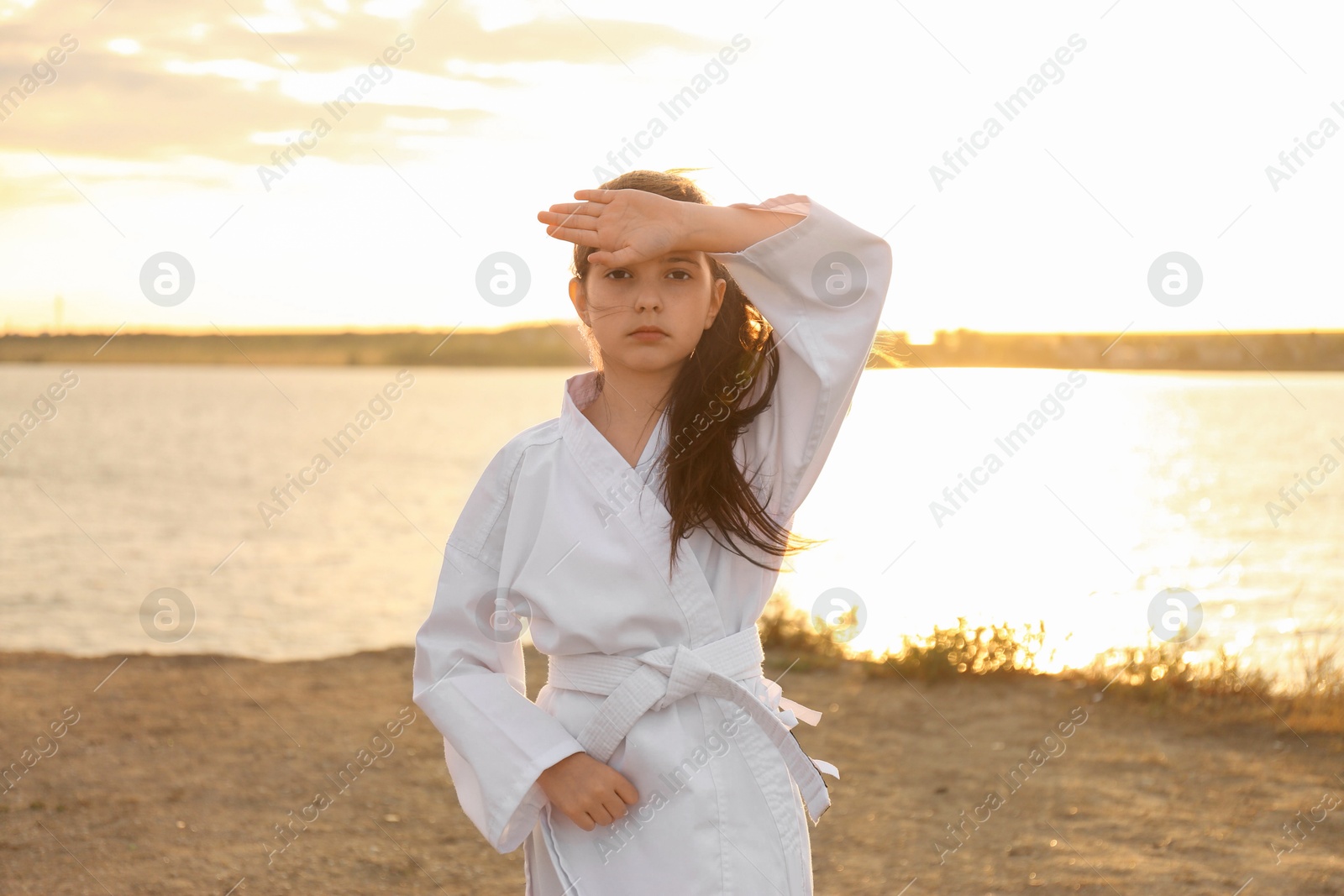 Photo of Cute little girl in kimono practicing karate near river at sunset