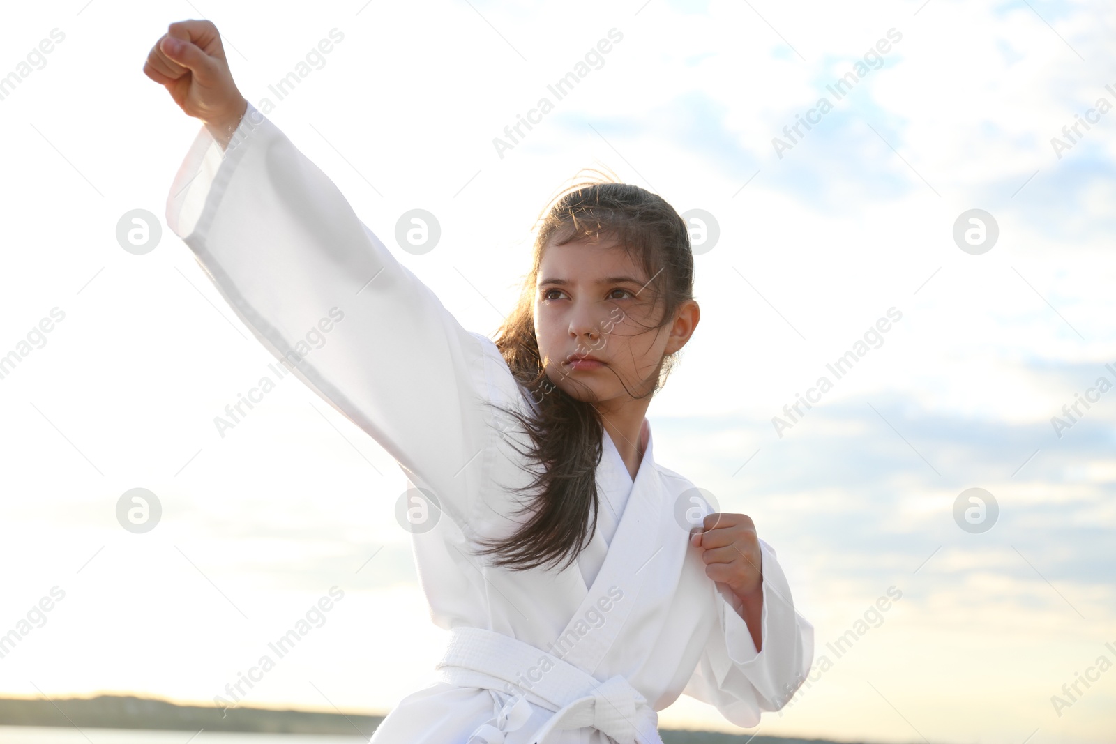 Photo of Cute little girl in kimono practicing karate outdoors on sunny day