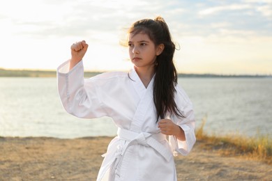 Cute little girl in kimono practicing karate near river on sunny day