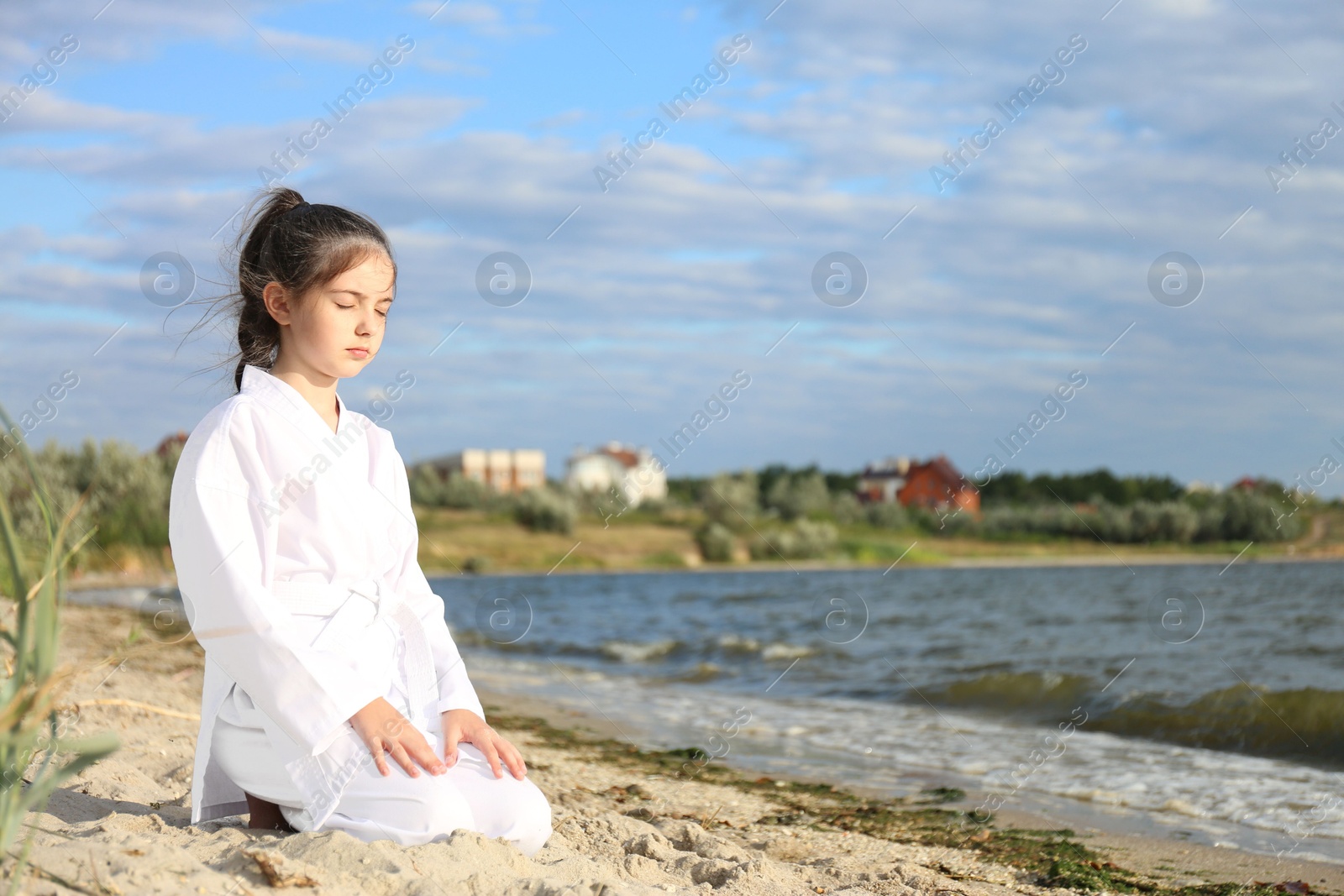 Photo of Cute little girl in kimono meditating near river. Karate practicing