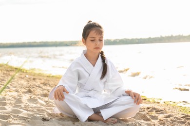 Photo of Cute little girl in kimono meditating near river. Karate practicing