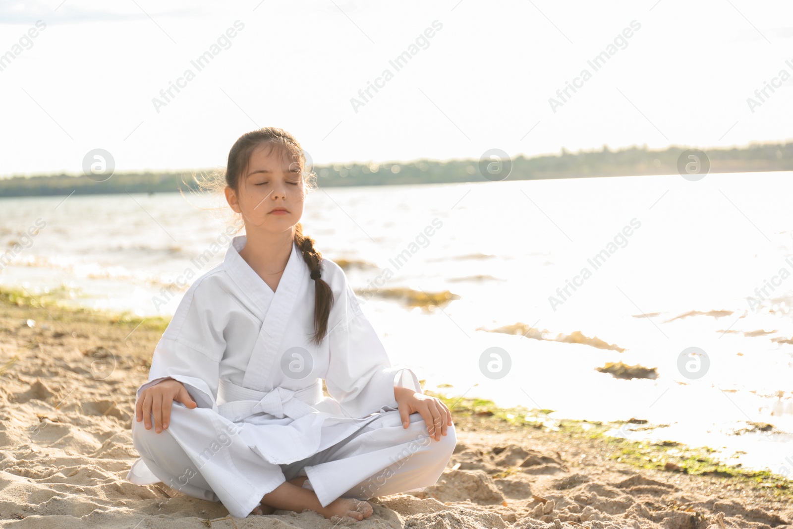 Photo of Cute little girl in kimono meditating near river. Karate practicing