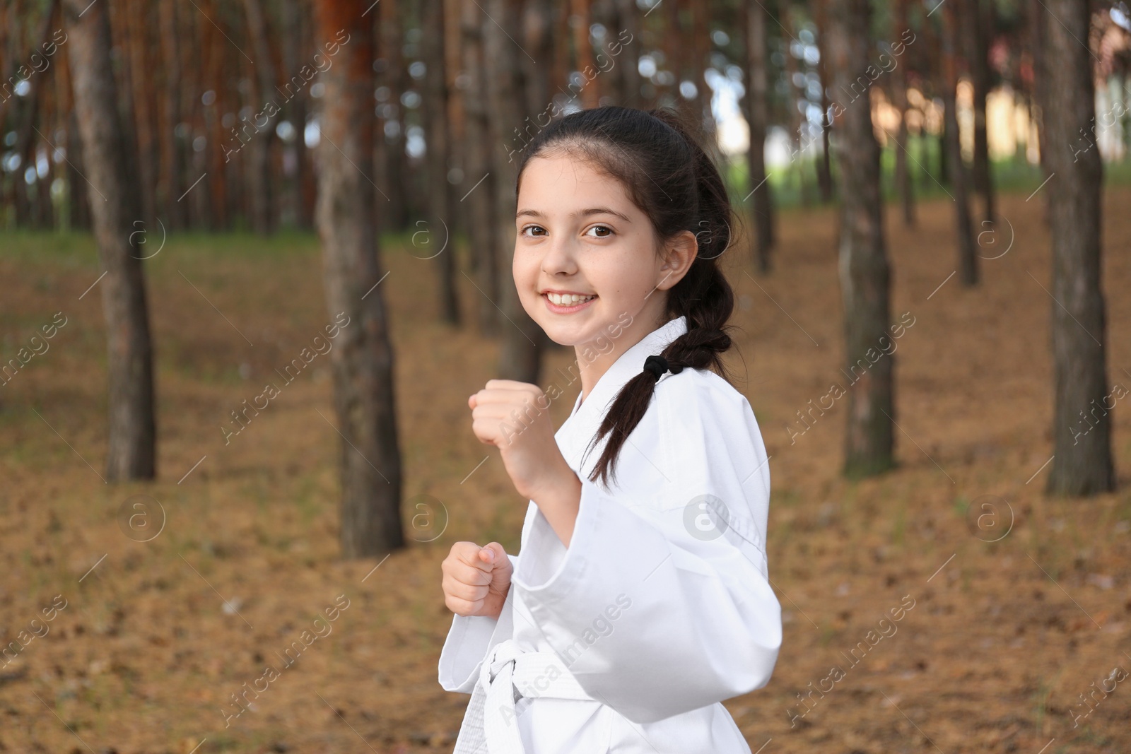 Photo of Cute little girl in kimono practicing karate in forest