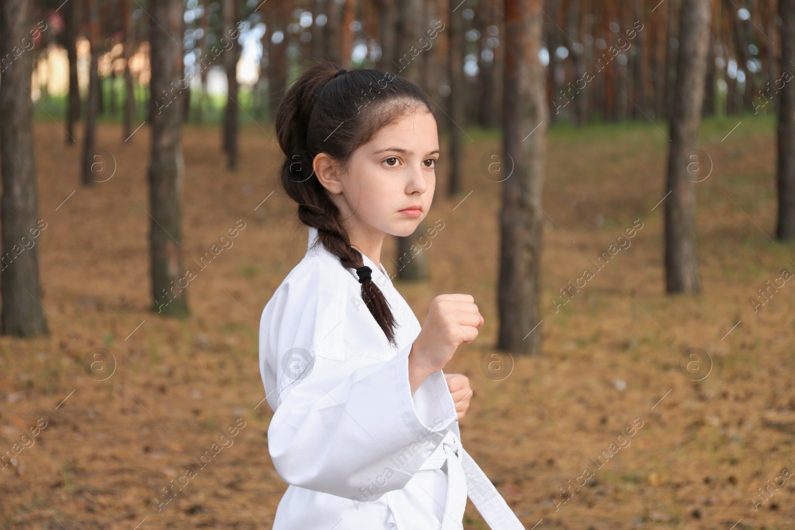 Photo of Cute little girl in kimono practicing karate in forest