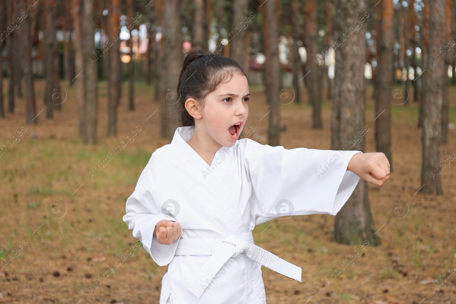 Photo of Cute little girl in kimono practicing karate in forest