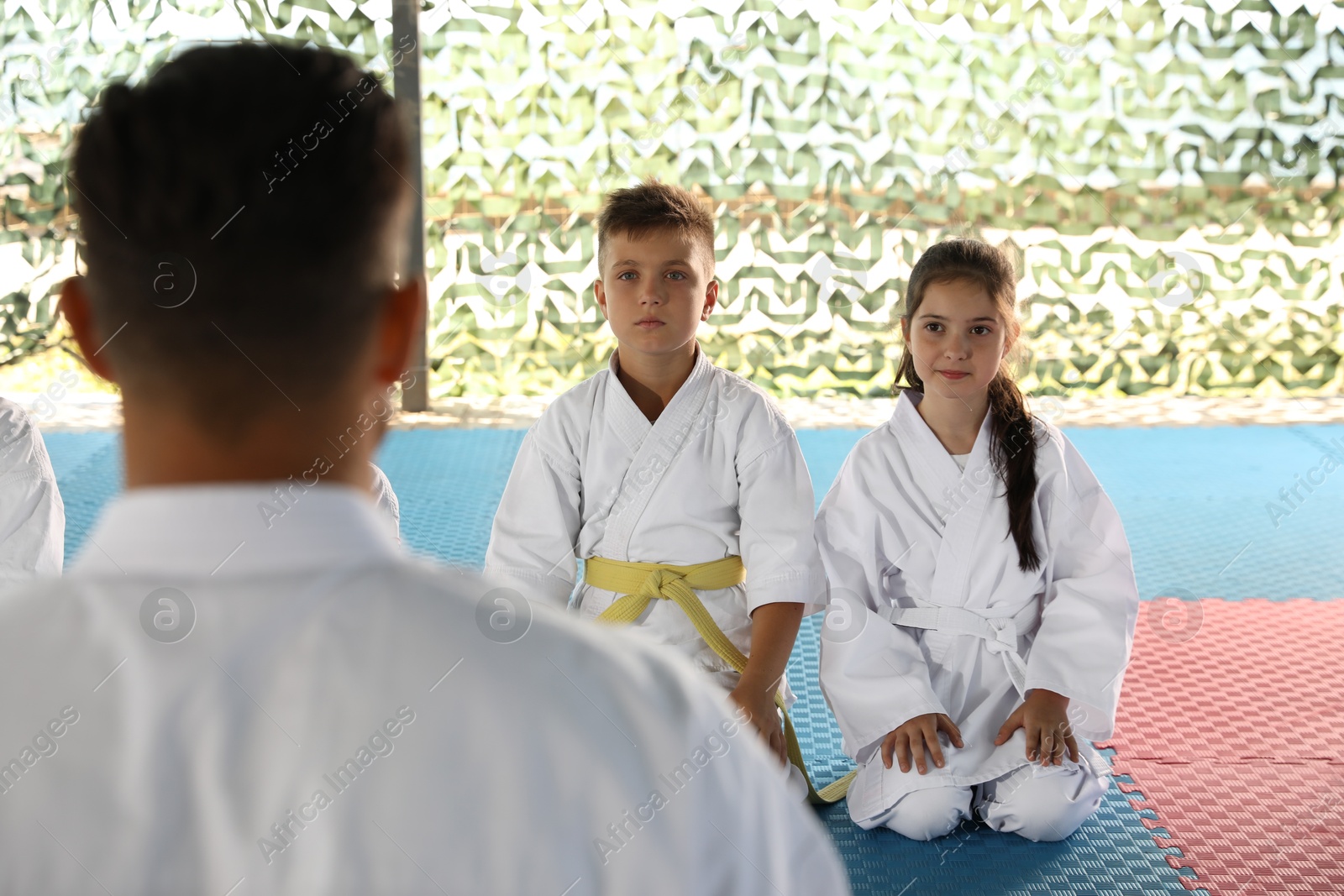 Photo of Children and coach sitting on tatami outdoors. Karate practice