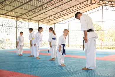 Photo of Children and coach in kimono performing ritual bow before karate practice on tatami outdoors