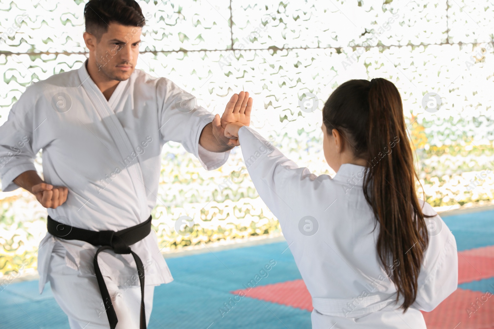 Photo of Girl practicing karate with coach on tatami outdoors