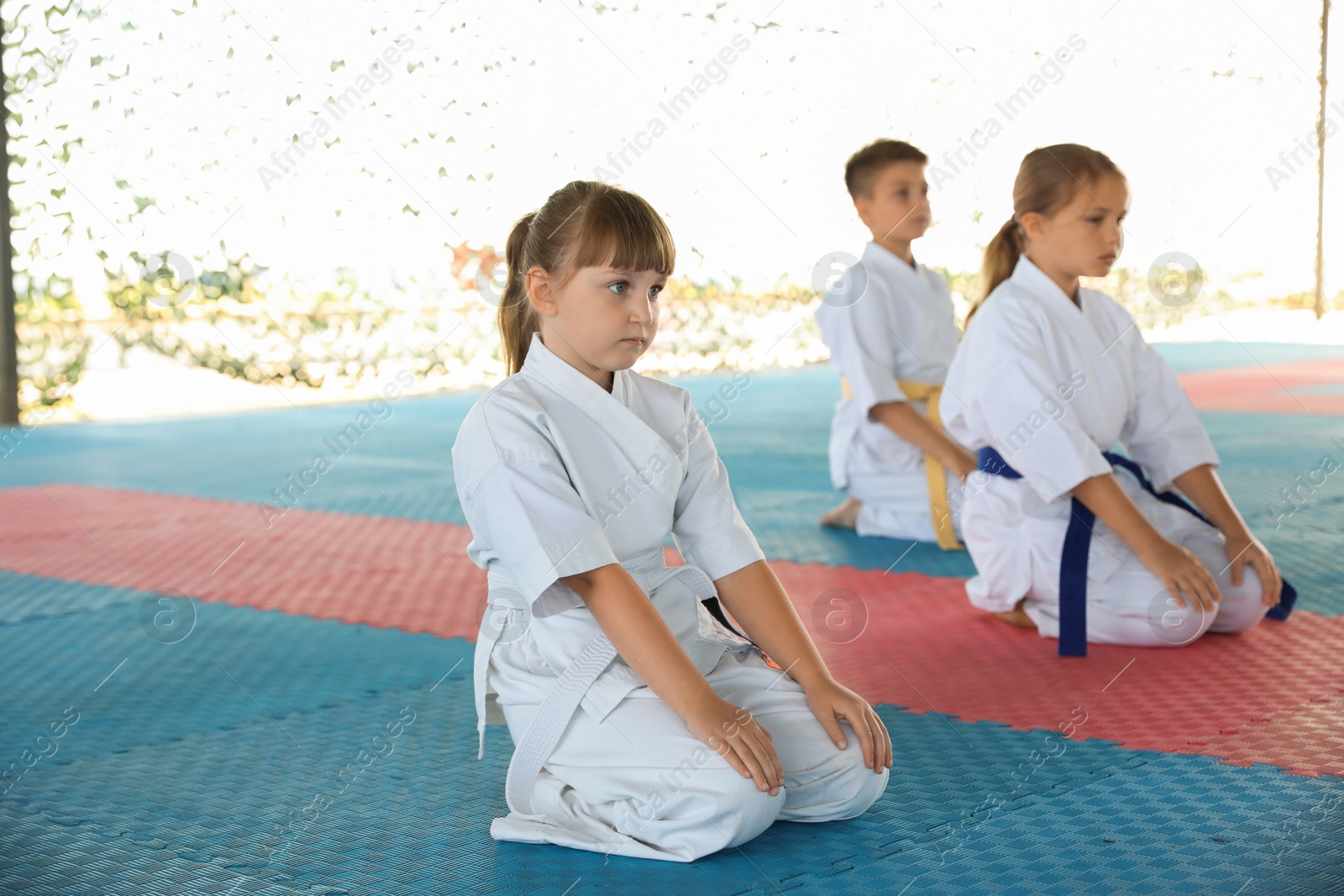 Photo of Children in kimono sitting on tatami outdoors. Karate practice