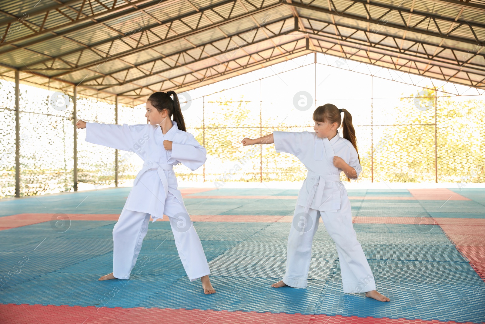 Photo of Children in kimono practicing karate on tatami outdoors