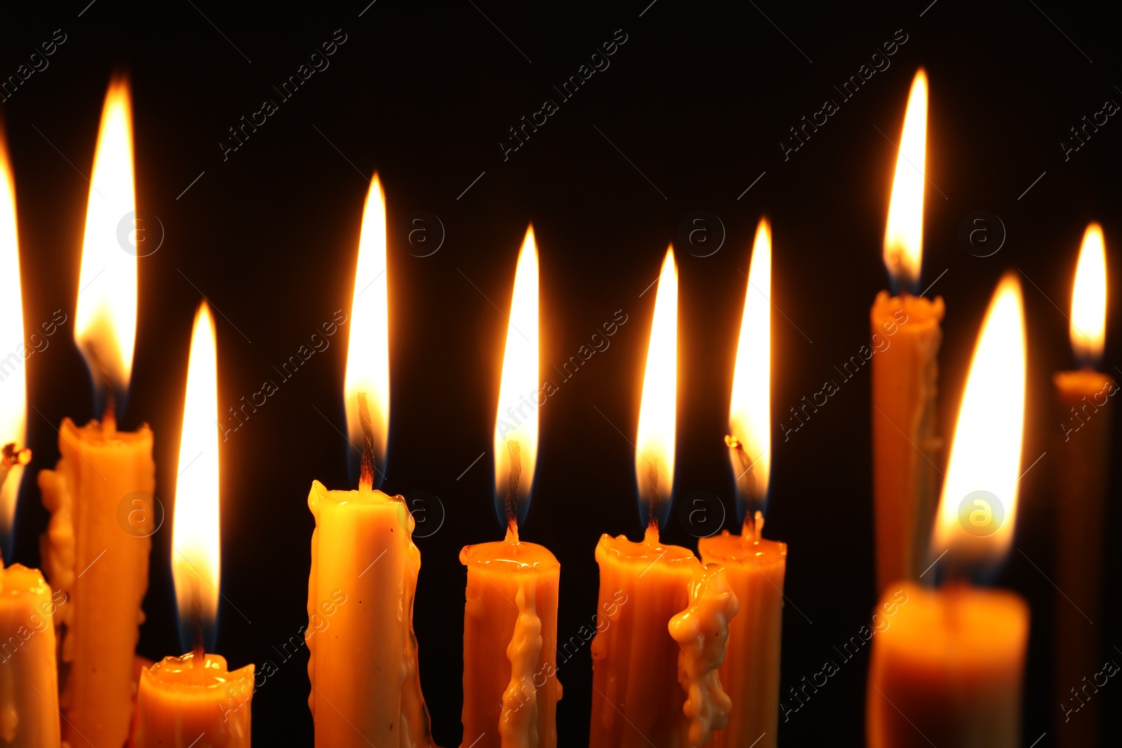 Photo of Many burning church candles on black background, closeup