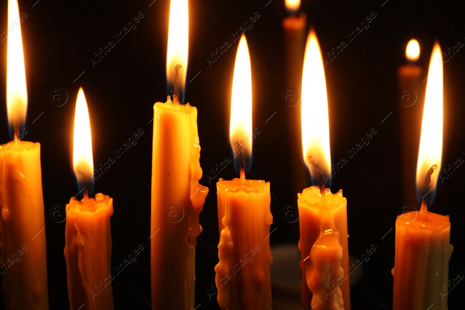 Photo of Many burning church candles on black background, closeup