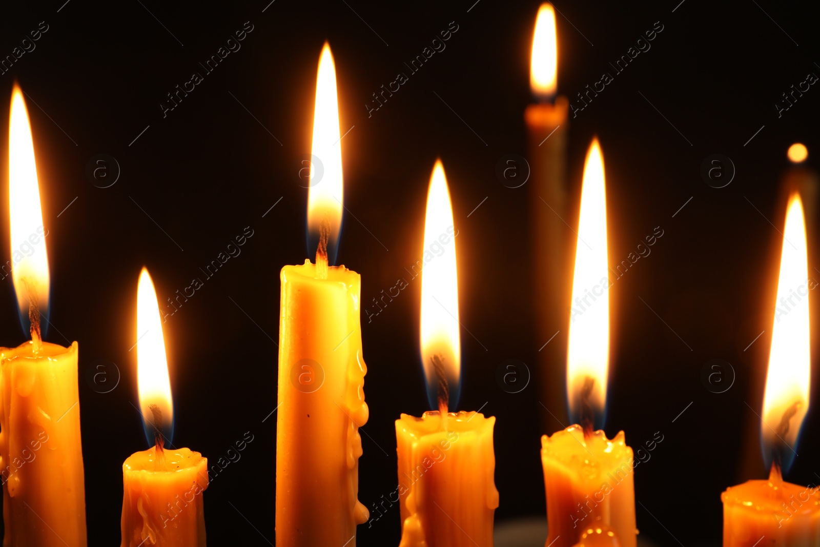 Photo of Many burning church candles on black background, closeup