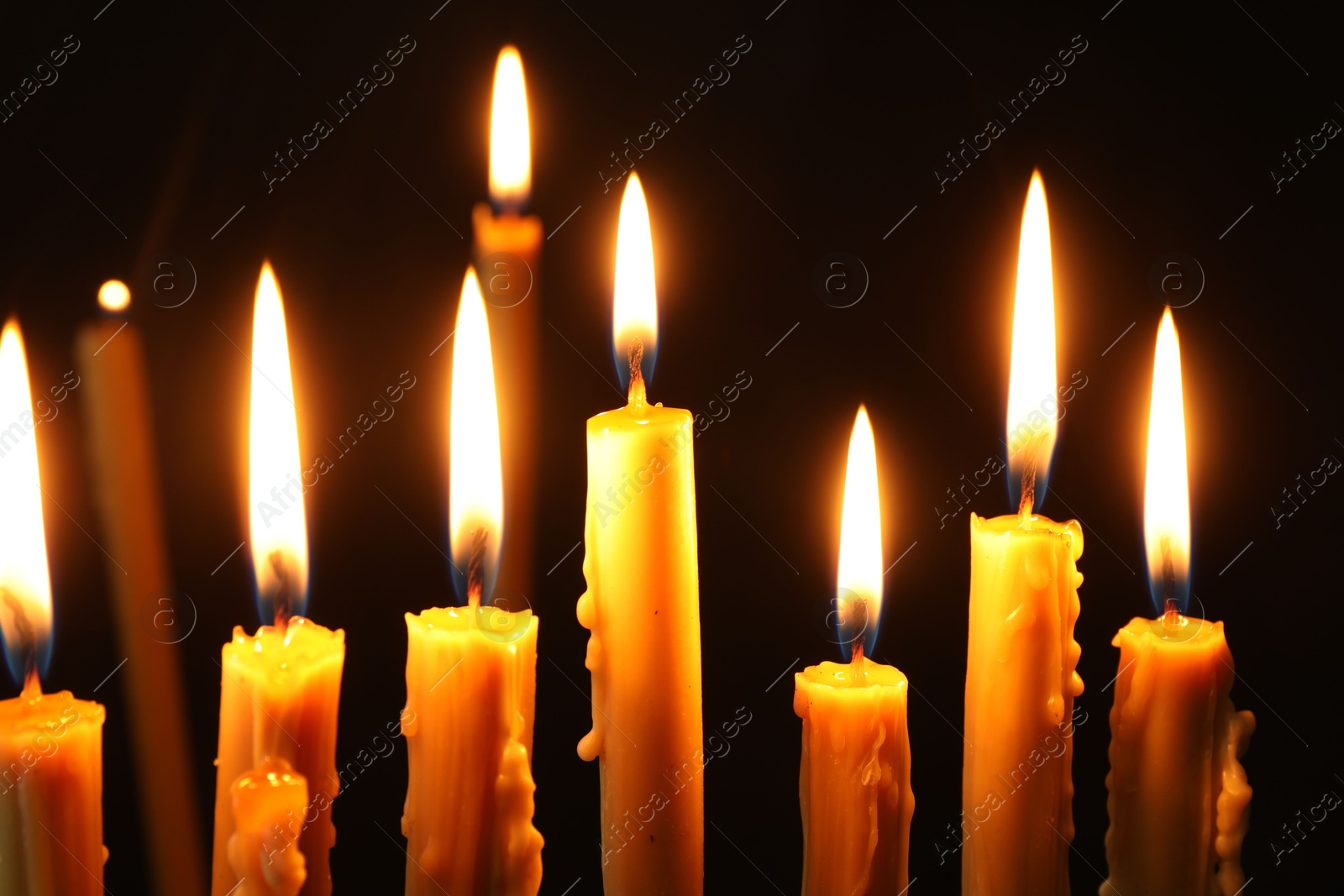 Photo of Many burning church candles on black background, closeup