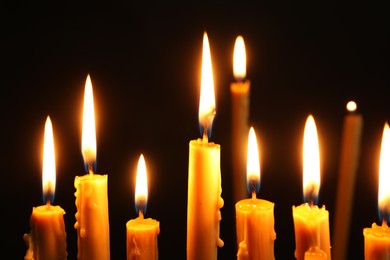 Photo of Many burning church candles on black background, closeup