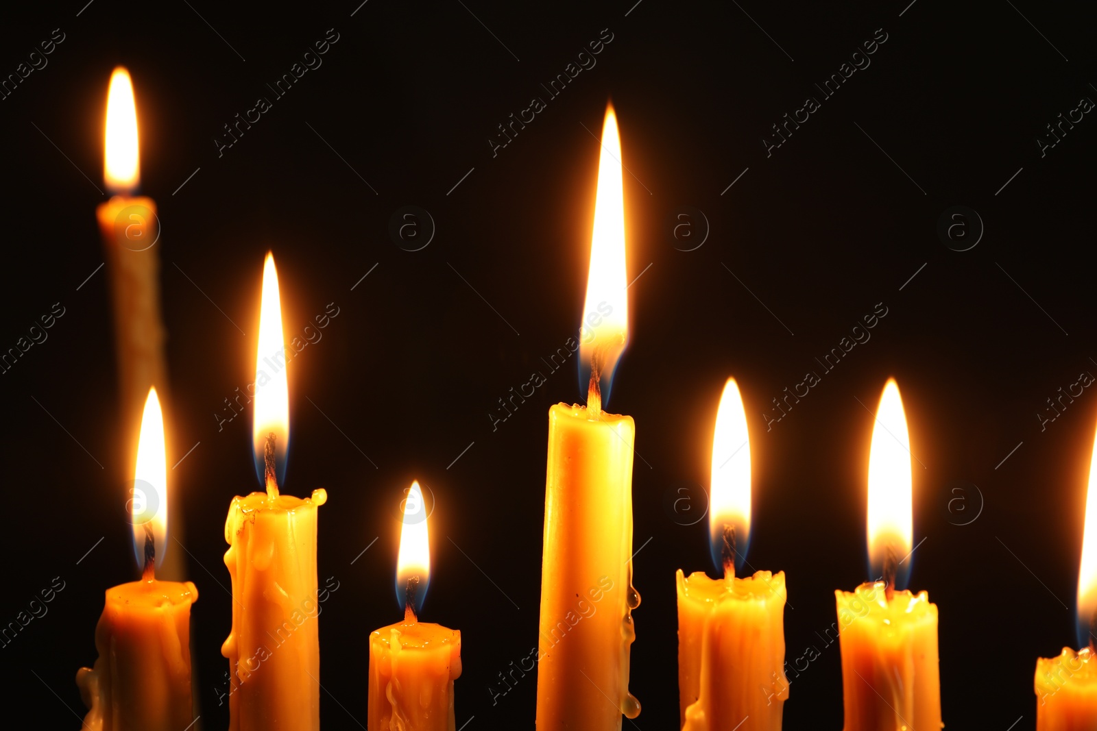 Photo of Many burning church candles on black background, closeup