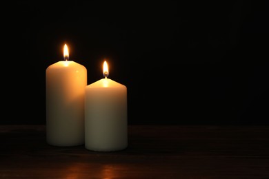 Photo of Two burning church candles on black background, space for text