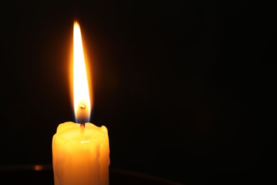 Photo of One burning church candle on black background, closeup. Space for text