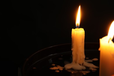 Photo of Two burning church candles on black background, space for text
