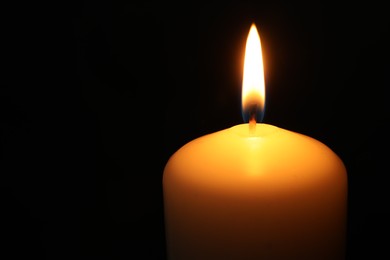 Photo of One burning church candle on black background, closeup. Space for text