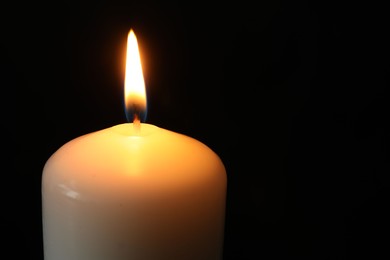 Photo of One burning church candle on black background, closeup. Space for text