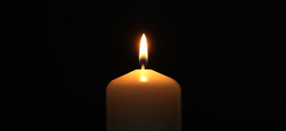 Photo of One burning church candle on black background, closeup