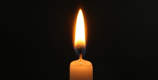 Photo of One burning church candle on black background, closeup