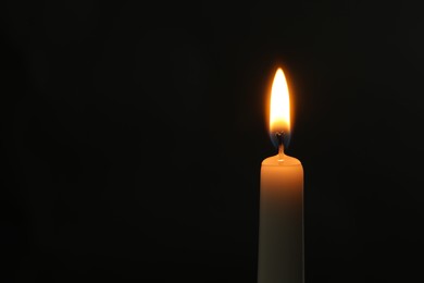 Photo of One burning church candle on black background, space for text
