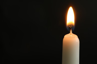 Photo of One burning church candle on black background, closeup. Space for text