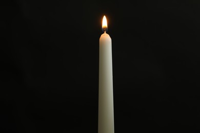 Photo of One burning church candle on black background