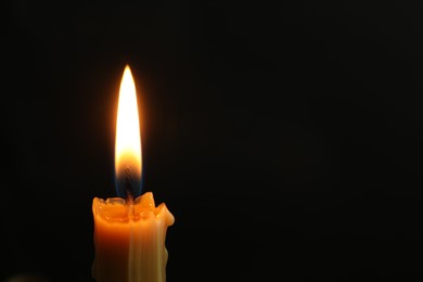 Photo of One burning church candle on black background, closeup. Space for text