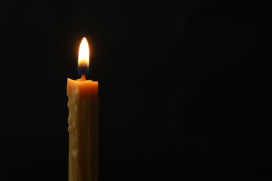 Photo of One burning church candle on black background, space for text