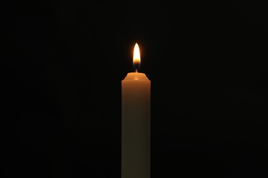 Photo of One burning church candle on black background