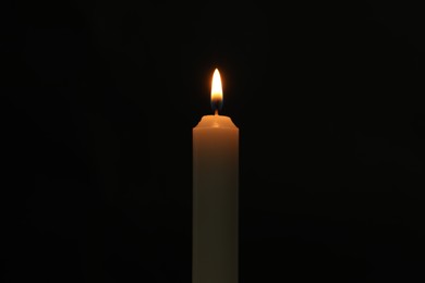 One burning church candle on black background