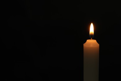 Photo of One burning church candle on black background, space for text