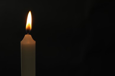 One burning church candle on black background, space for text