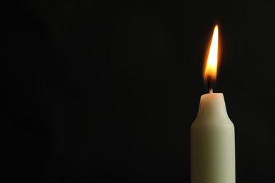 Photo of One burning church candle on black background, closeup. Space for text