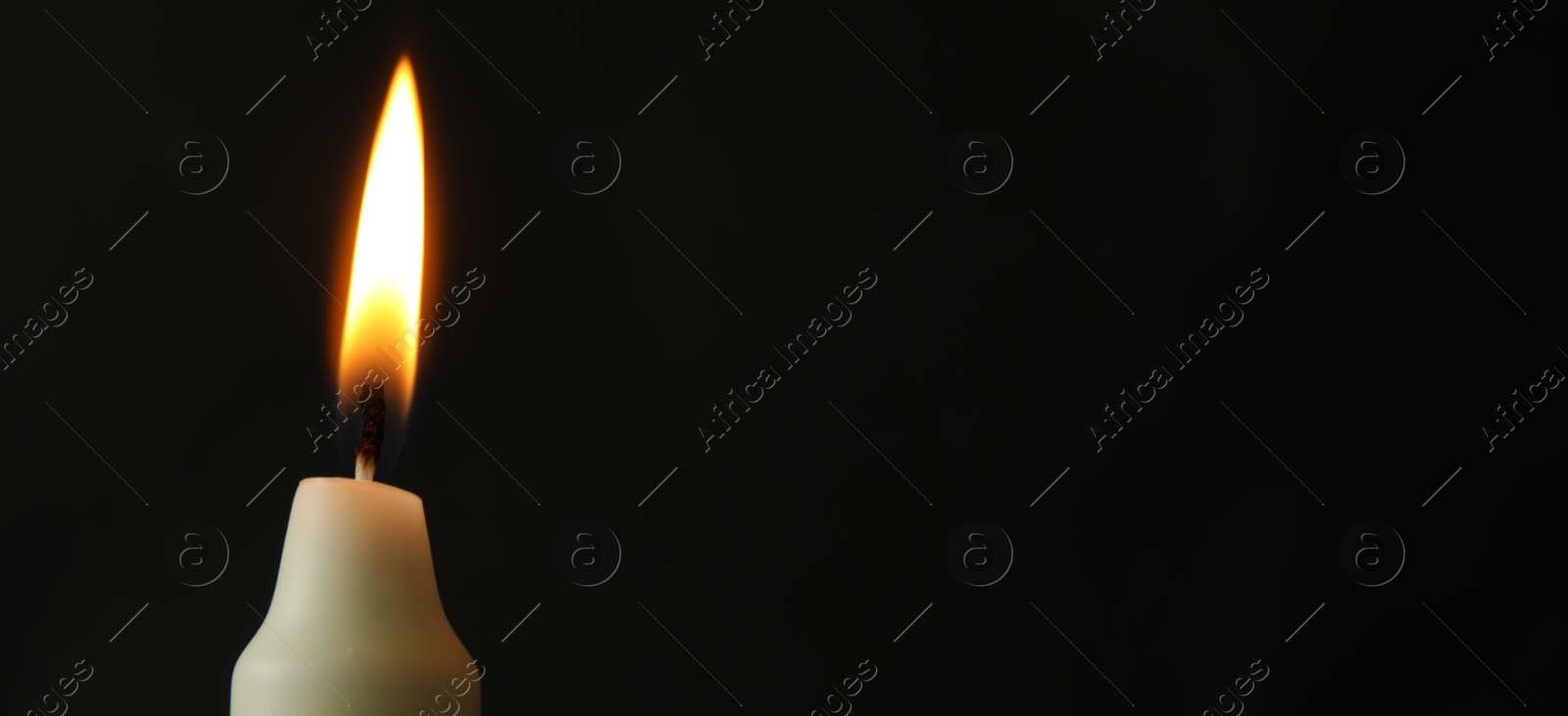 Photo of One burning church candle on black background, closeup. Space for text