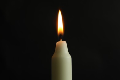 Photo of One burning church candle on black background, closeup