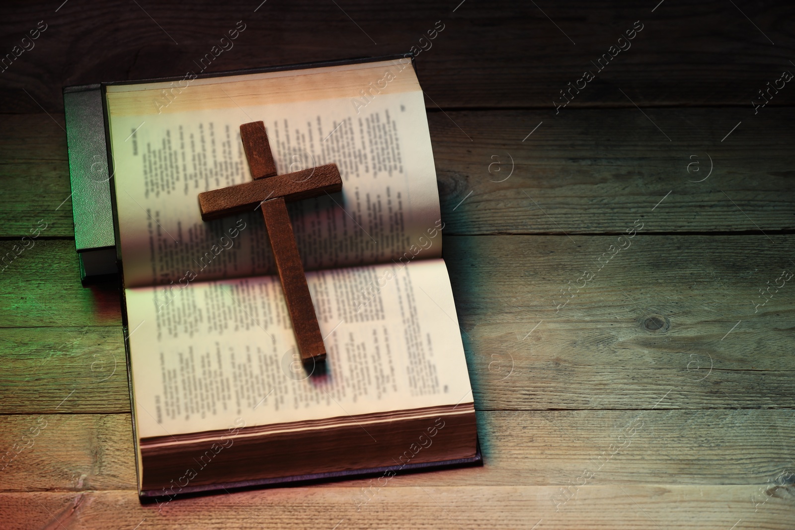 Photo of Cross and Bible on wooden table in color lights, top view with space for text. Religion of Christianity