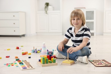 Cute little boy playing with toy pyramid on floor indoors